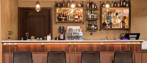 Zona de bar con paneles de madera, barra con varias botellas, máquina de café y taburetes.