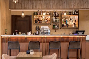 A bar area with wooden paneling, a counter with various bottles, a coffee machine, and bar stools.