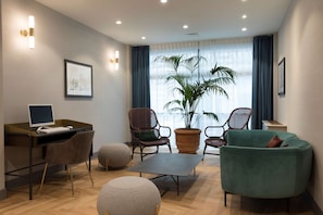 A modern living room with a desk, two chairs, a sofa, a potted plant, and a large window with curtains.
