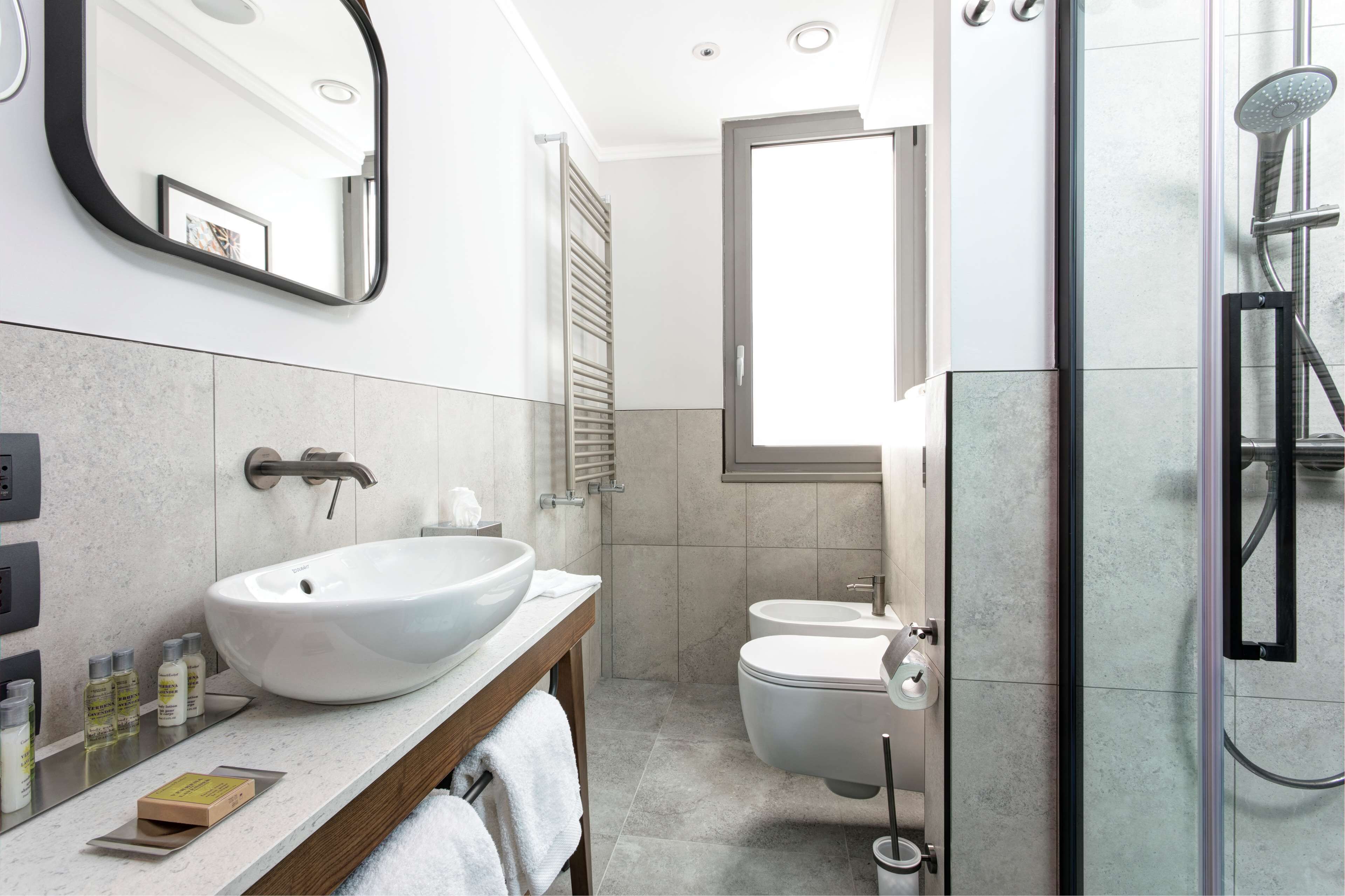Un baño moderno con un lavamanos grande de color blanco, un inodoro y una zona de ducha con mampara de vidrio.