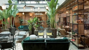 Recepció d'hotel amb sostre de vidre, plantes d'interior, zones de seients i una prestatgeria de fusta.
