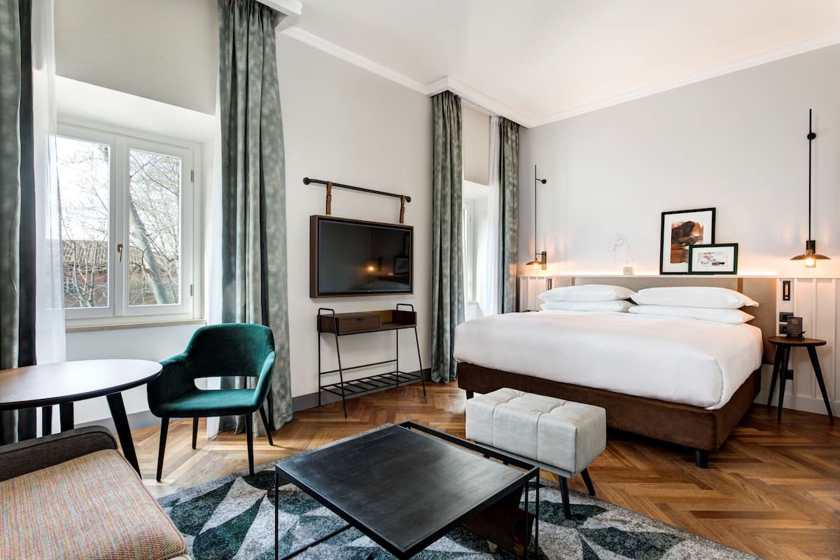 A hotel room with a bed, a desk, a chair, a TV, and a bedside table.