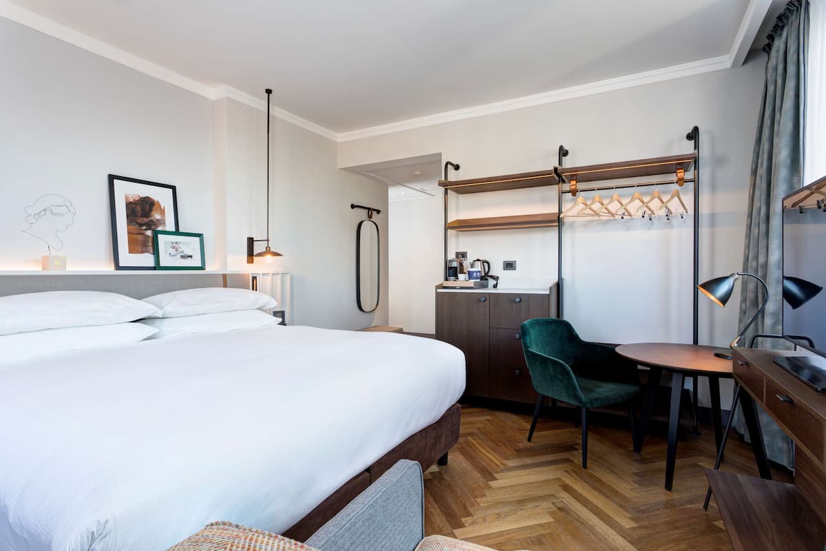 Una habitación de hotel con cama, escritorio, silla y perchero.