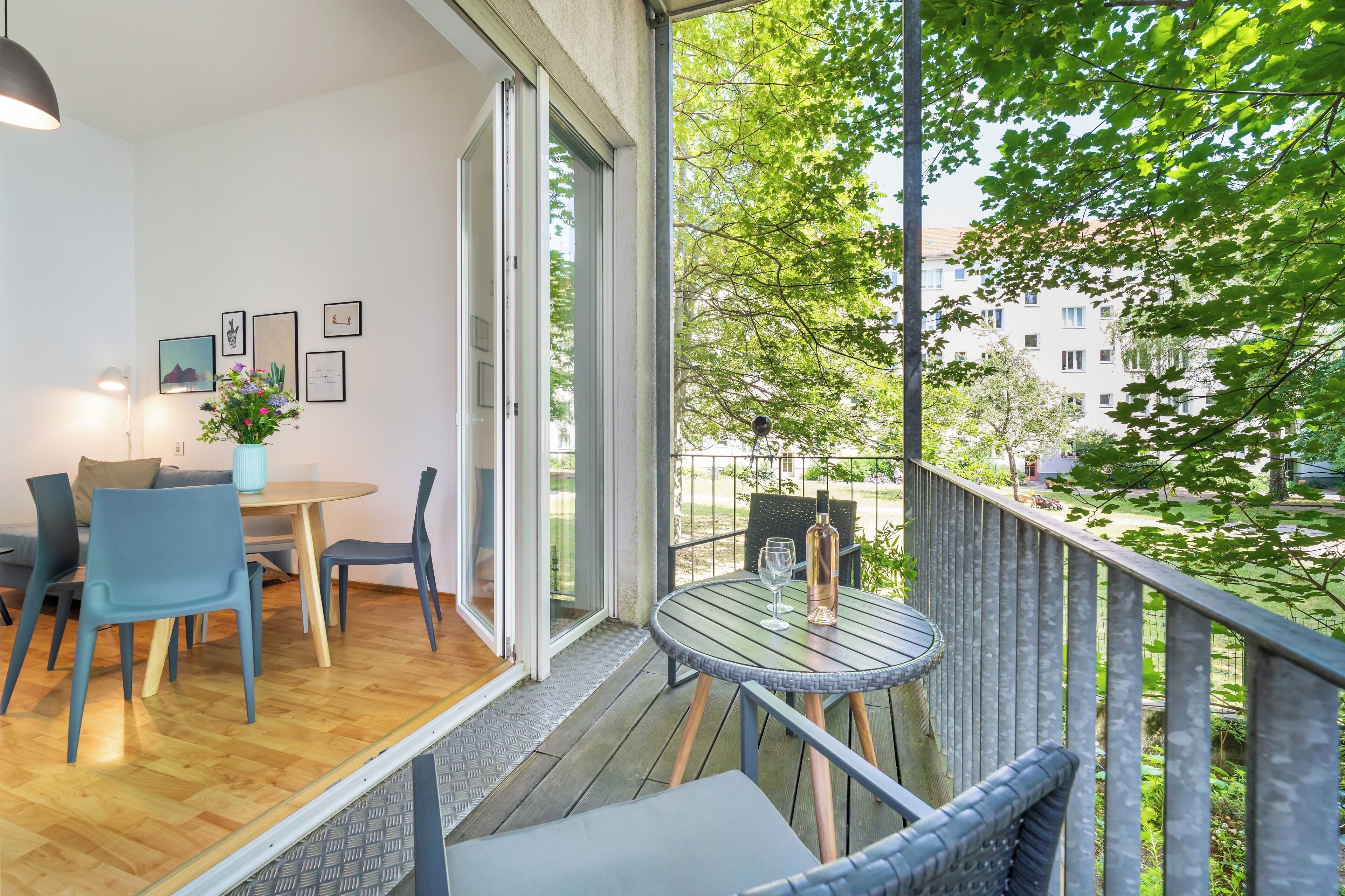 A balcony with a table and chairs, a potted plant, and a view of a building and trees.