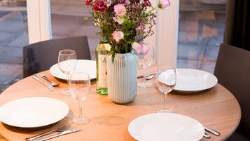 Una mesa de comedor dispuesta con platos, cubiertos, copas de vino y un florero con flores.