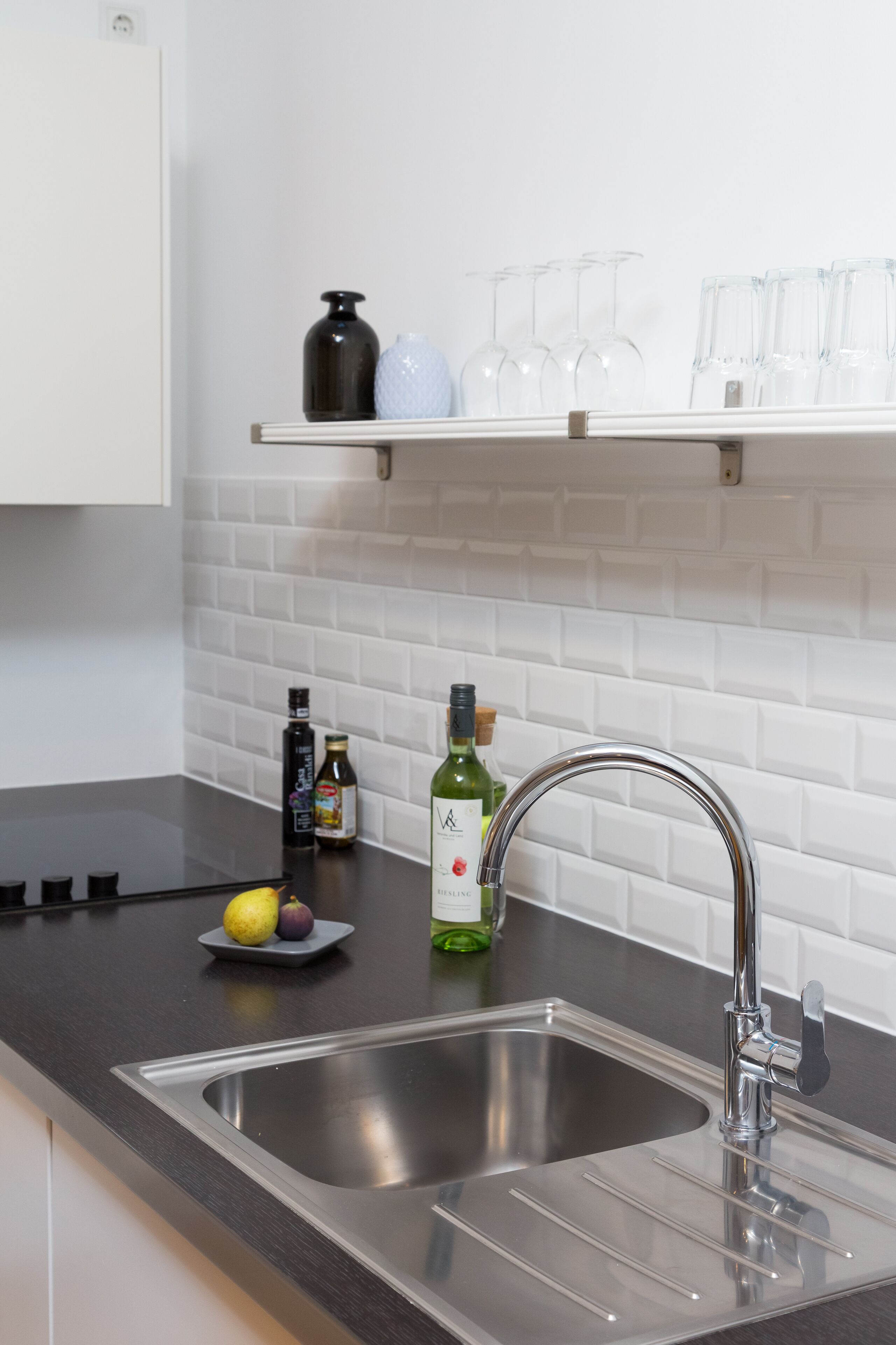 A modern kitchen with a stainless steel sink, a black countertop, and a white tiled backsplash.