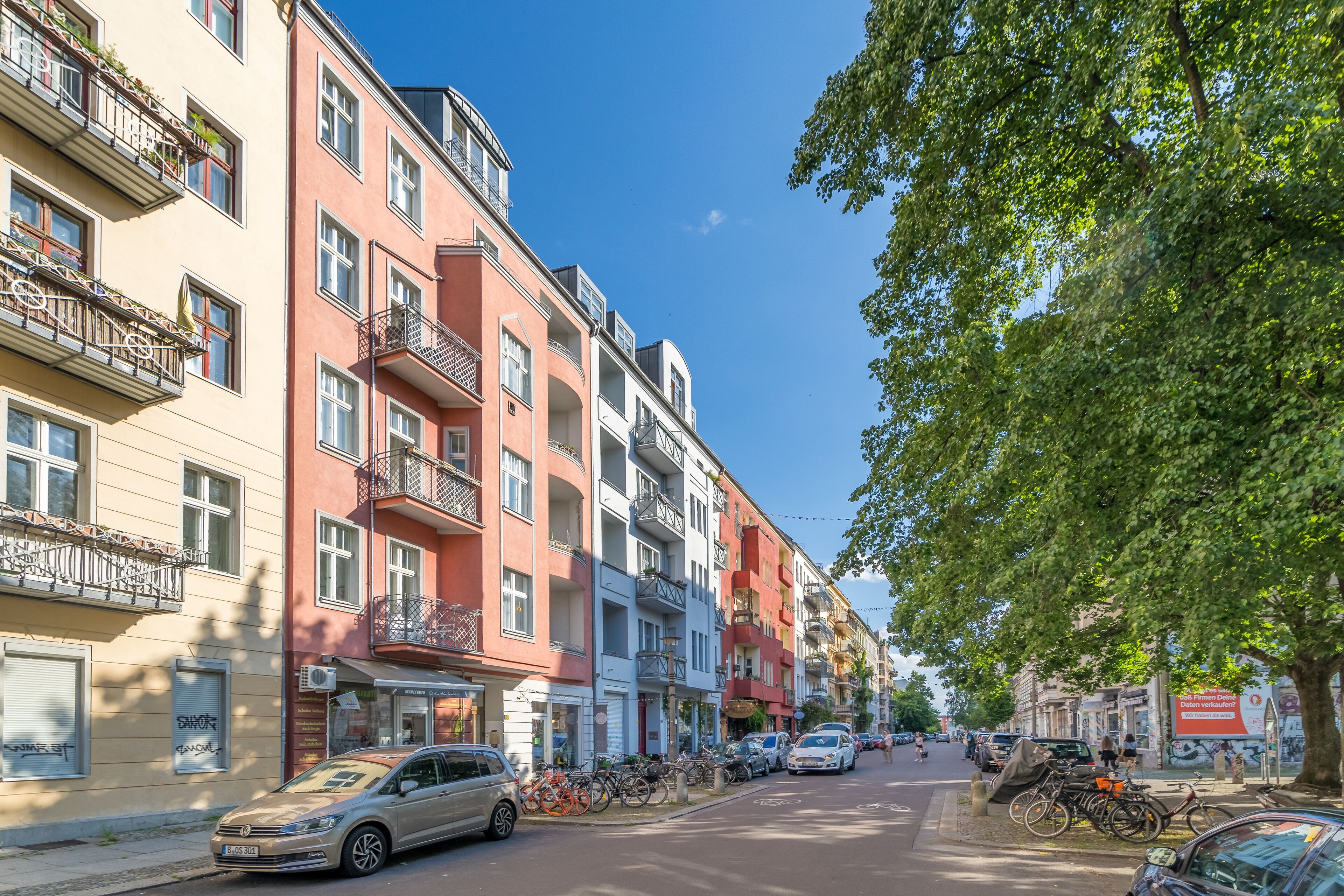 A street lined with multi-story buildings, some with balconies and others with ground-level shops.