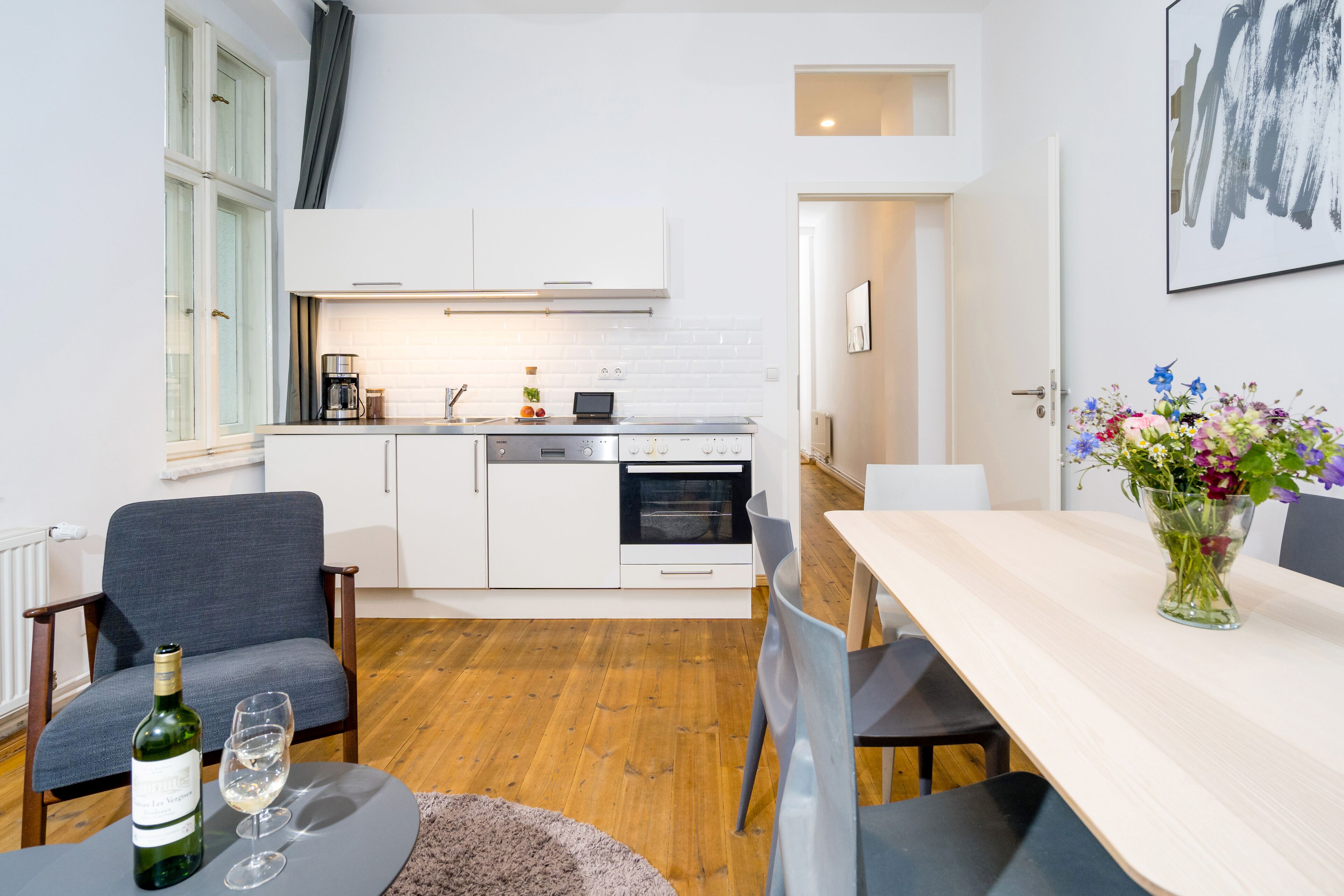 A modern kitchen with white cabinets, a dining area with a table and chairs, and a vase of flowers on the table.