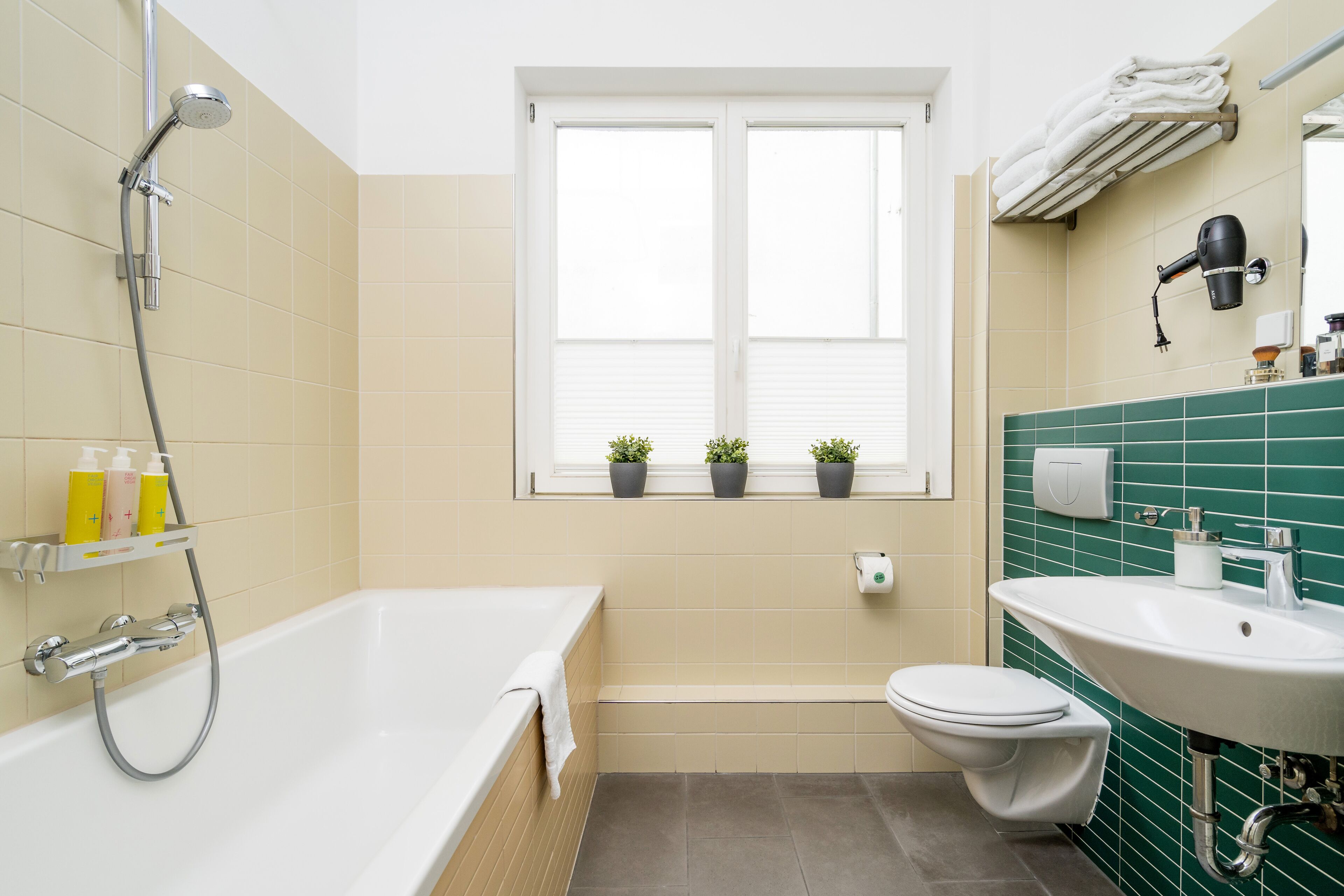 A bathroom with a bathtub, toilet, sink, and a window with potted plants.