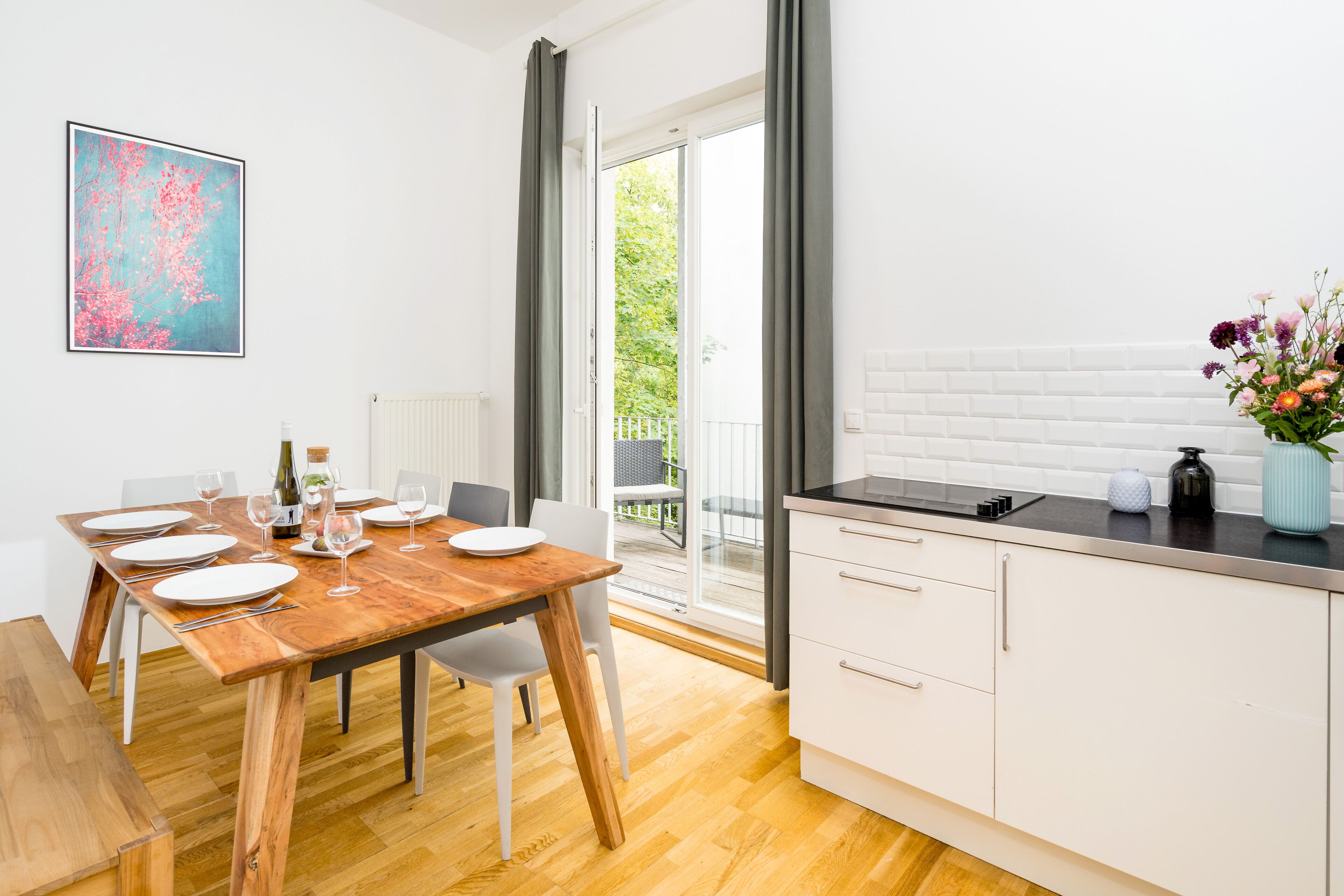 A modern kitchen with a wooden dining table set for four, white cabinets, and a view to the outside.