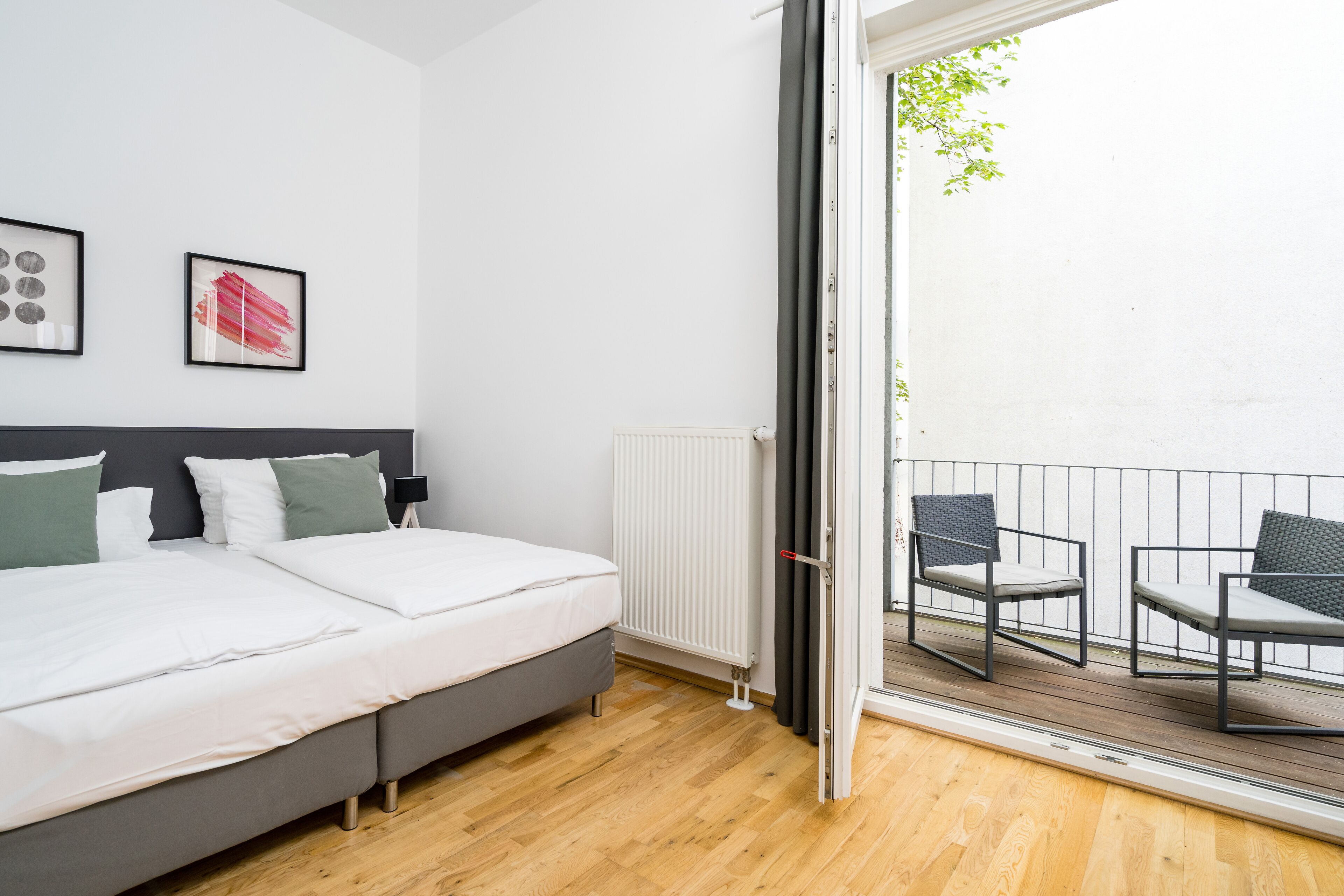 Un dormitorio con cama, radiador y balcón con sillas.