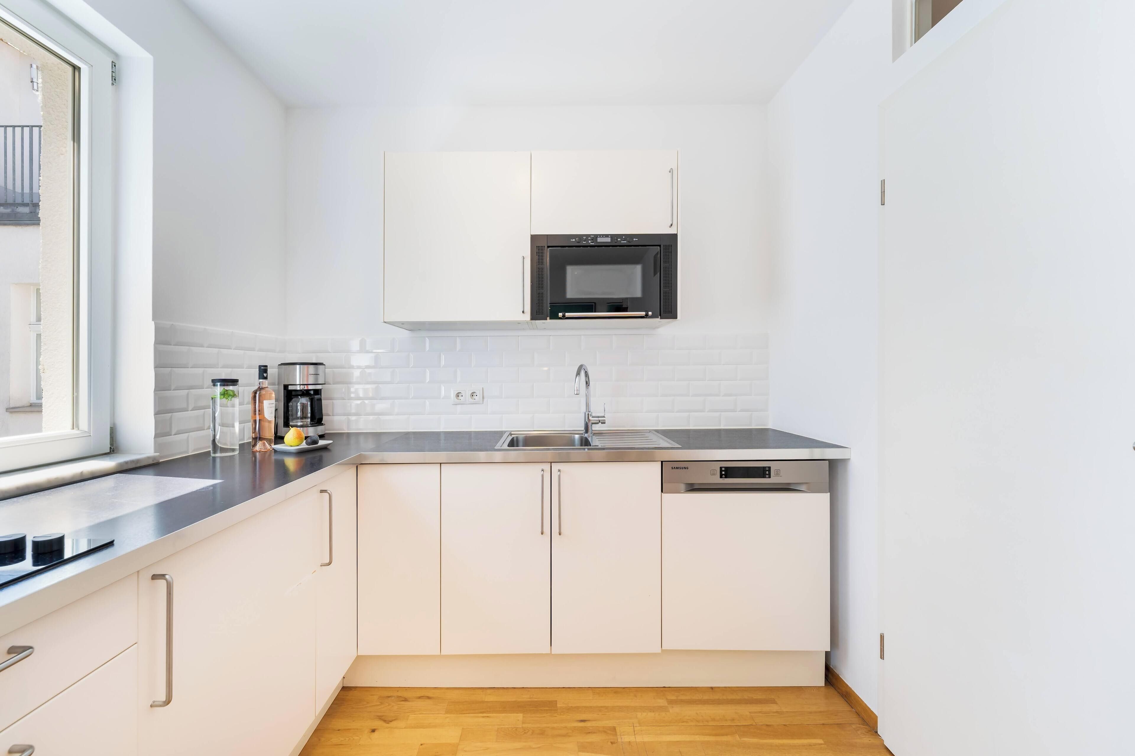 Una cocina compacta con armarios blancos, un microondas integrado, un lavabo y un lavavajillas.