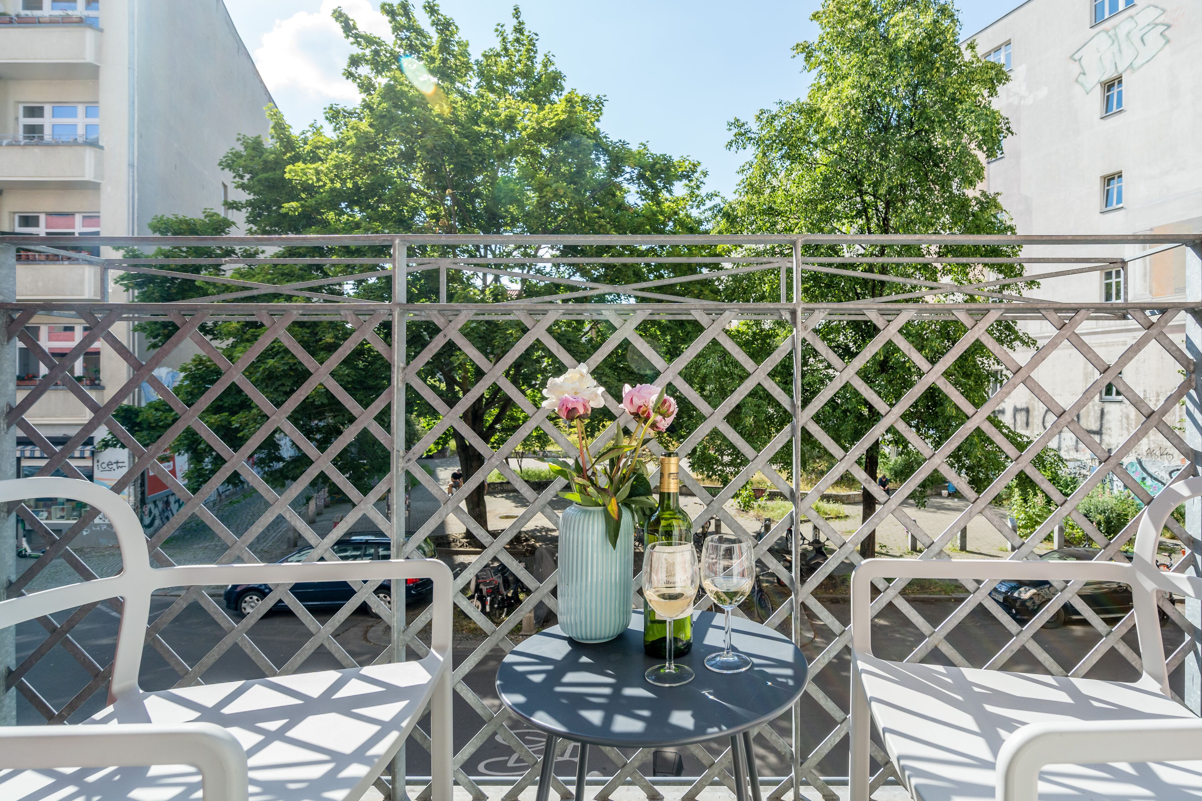Un balcon avec une table, des chaises, un vase rempli de fleurs et une bouteille de vin.