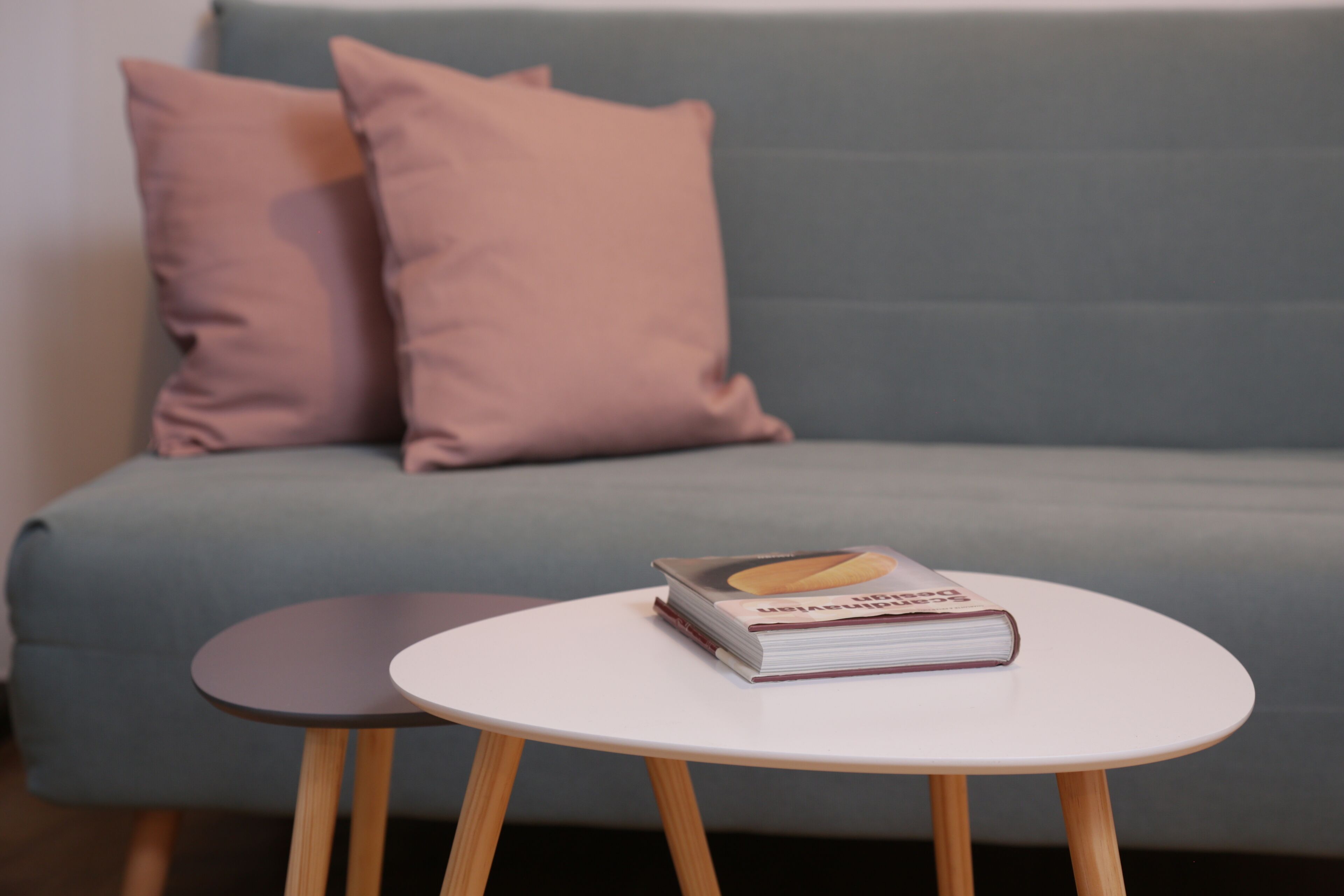 A modern living room with a light blue sofa, two pink pillows, and a white round table with a book on it.