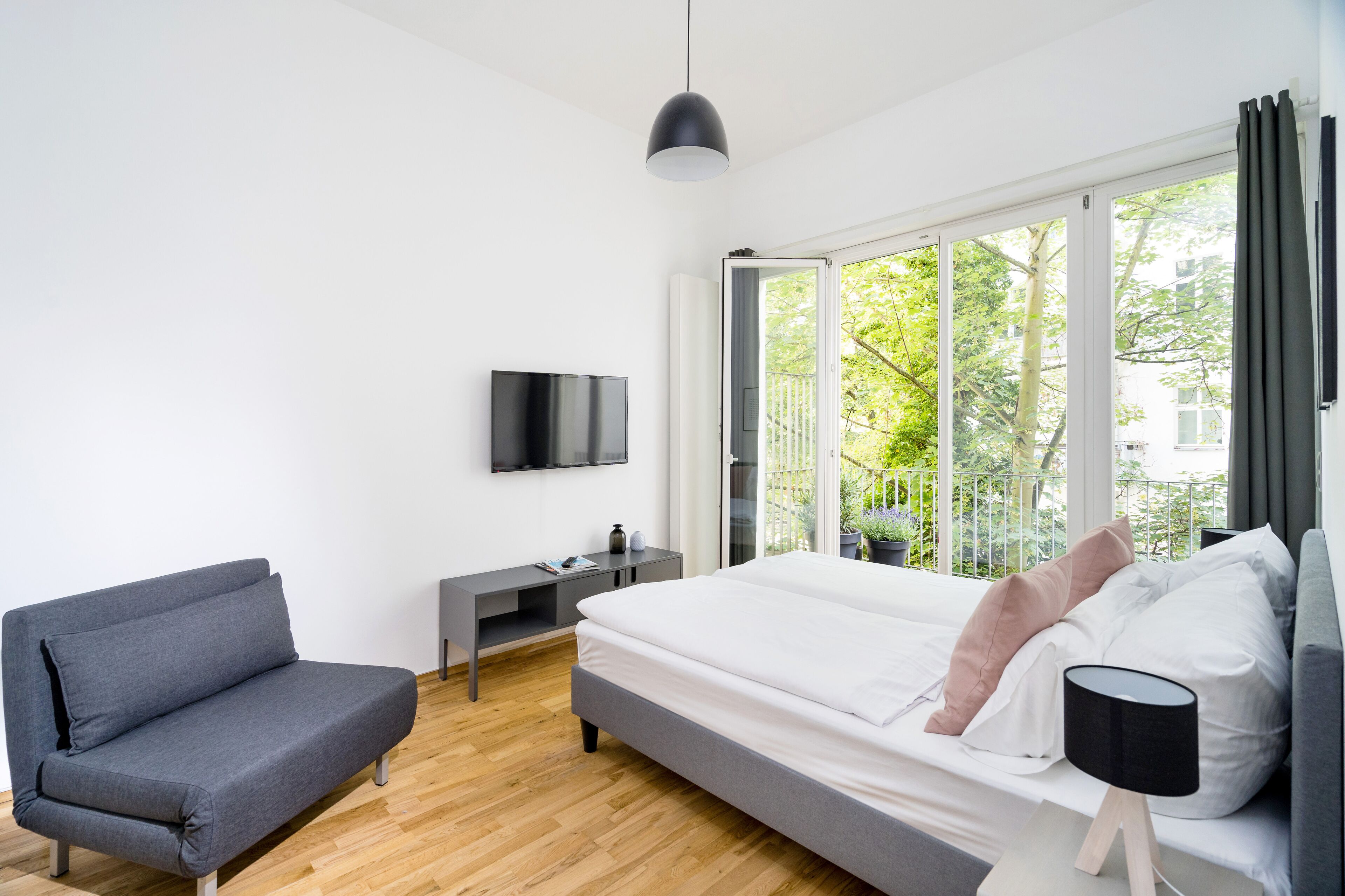 Ett modernt sovrum med en säng, en grå soffa, ett skrivbord och en tv.