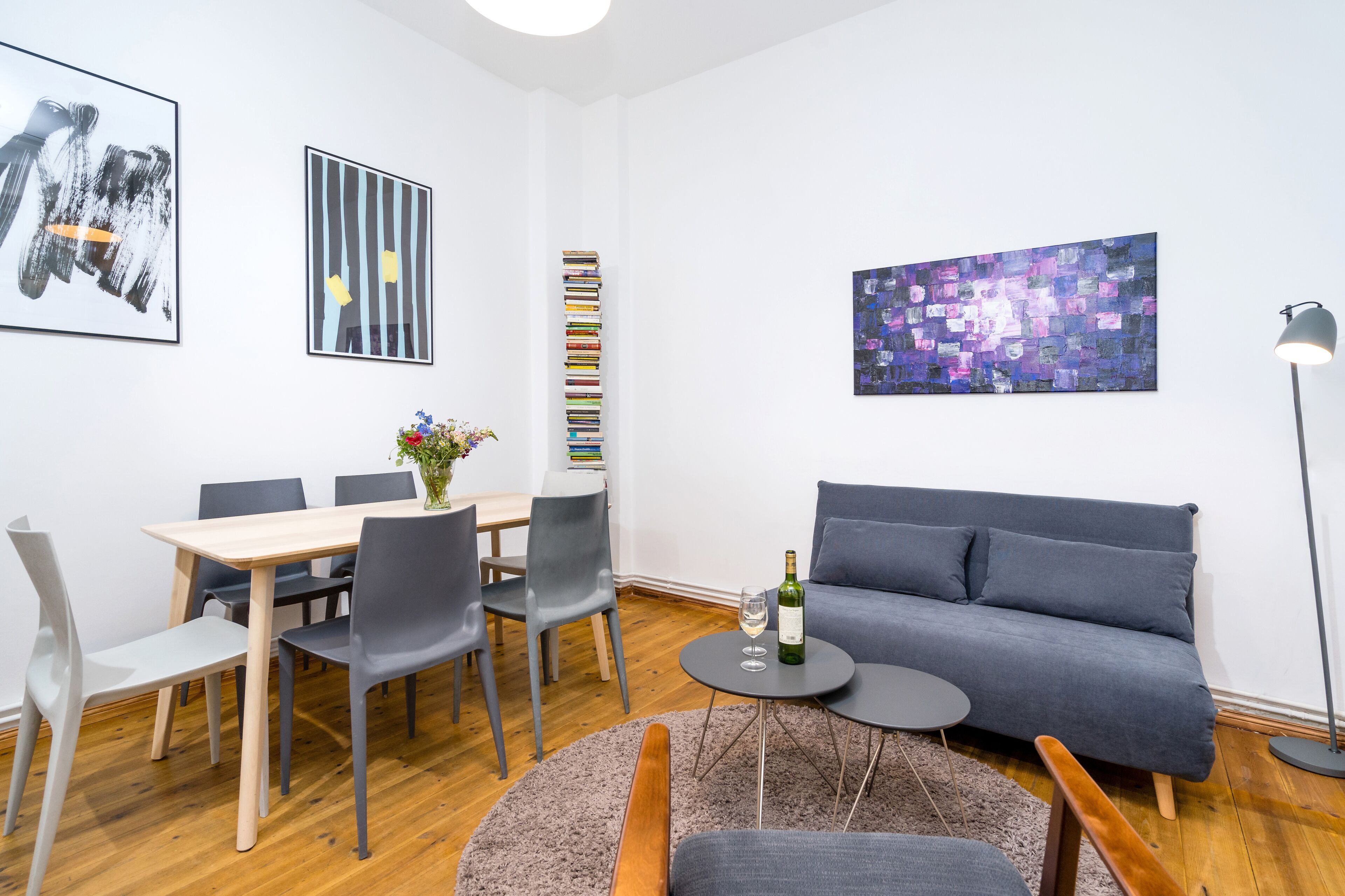 Un salon moderne avec un coin repas, un canapé gris et une bibliothèque.