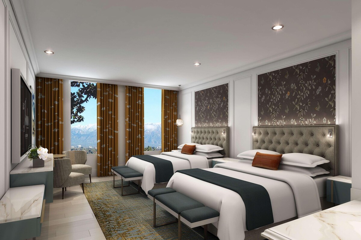 Una habitación de hotel moderna con dos camas, una zona de estar y vistas a montañas.