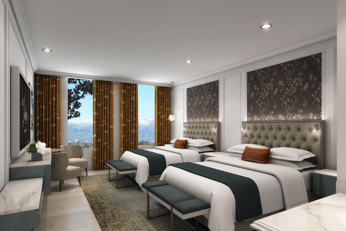 A modern hotel room with two beds, a seating area, and a large window with a mountain view.