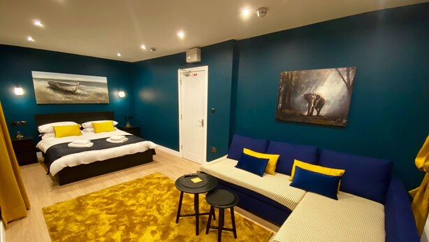 A modern bedroom with a bed, a sofa, a small table, and artwork on the walls. - Sky City Apartments (Coventry)