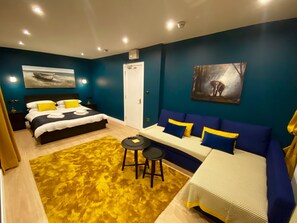 A modern bedroom with a bed, a sofa, a small table, and artwork on the walls. - Sky City Apartments (Coventry)