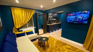 A modern hotel room with a bed, a small table, a TV, and a kitchenette. - Sky City Apartments (Coventry)