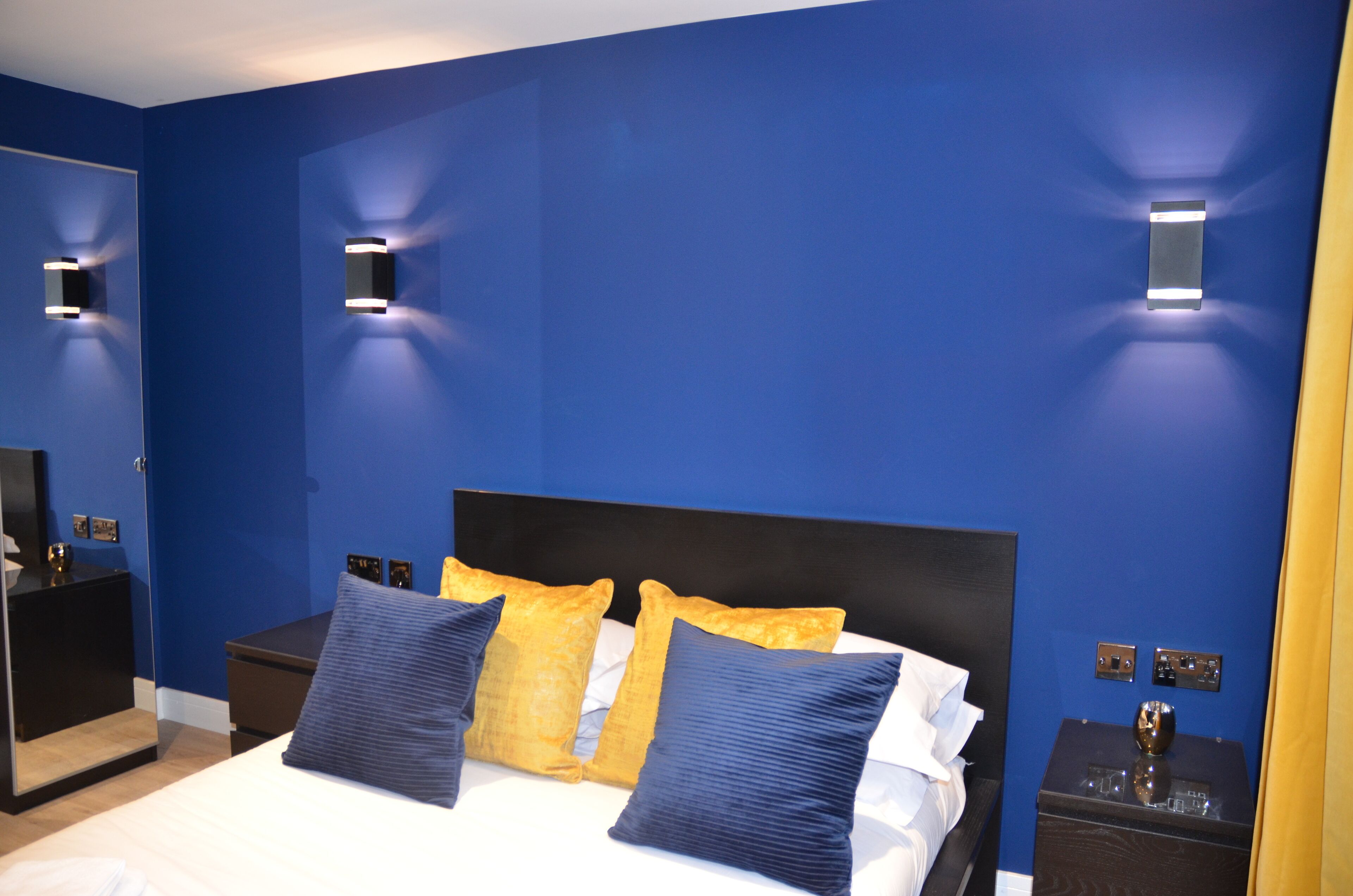A bedroom with a large bed, two bedside tables, and wall-mounted lights.
