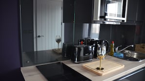 A modern kitchen with a glass countertop, a toaster, a wine glass, and a microwave. - Sky City Apartments (Coventry)