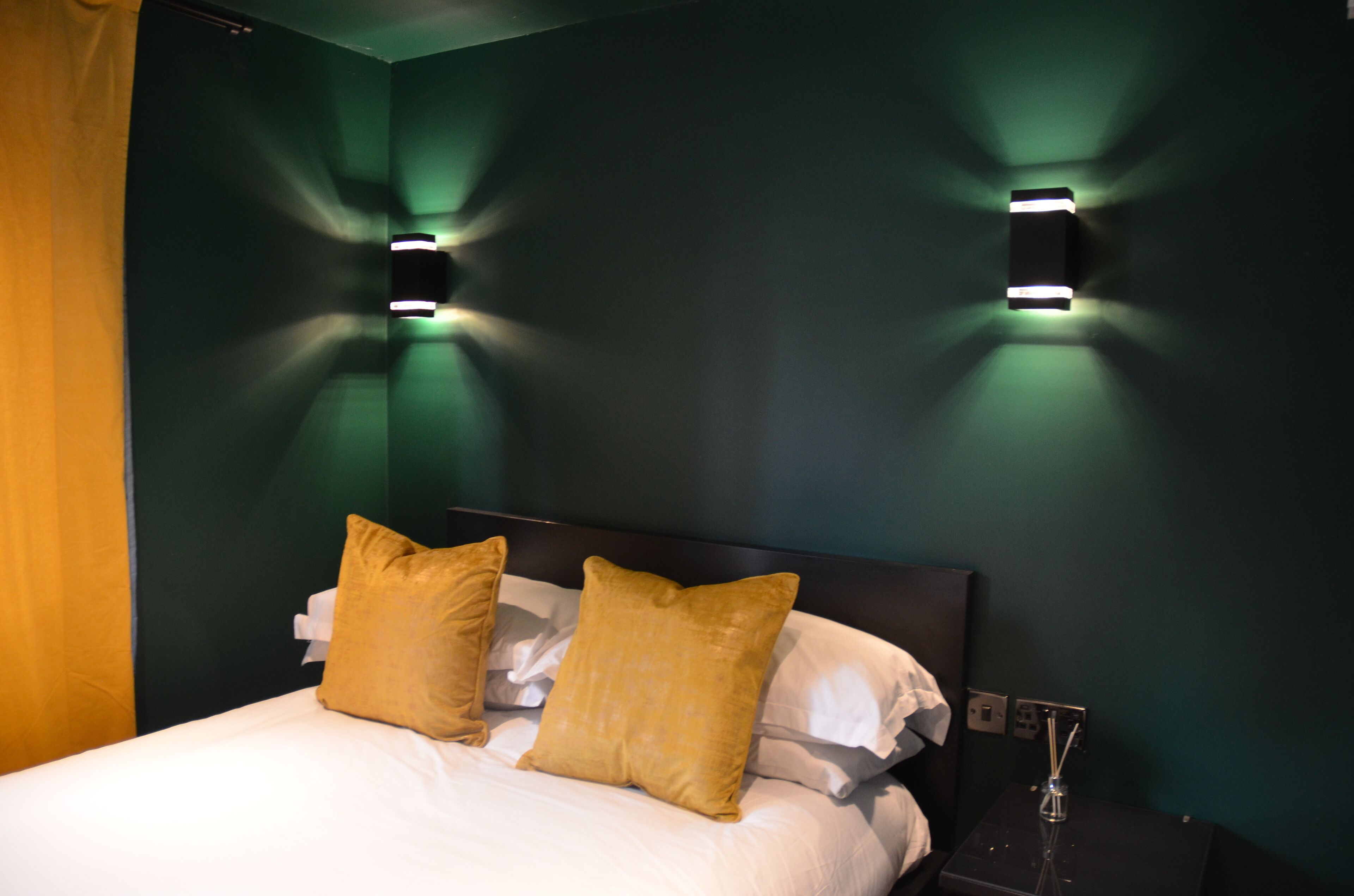 Une chambre d’hôtel avec un lit, deux lampes fixées au mur et une table de chevet sur laquelle se trouve un objet en verre.