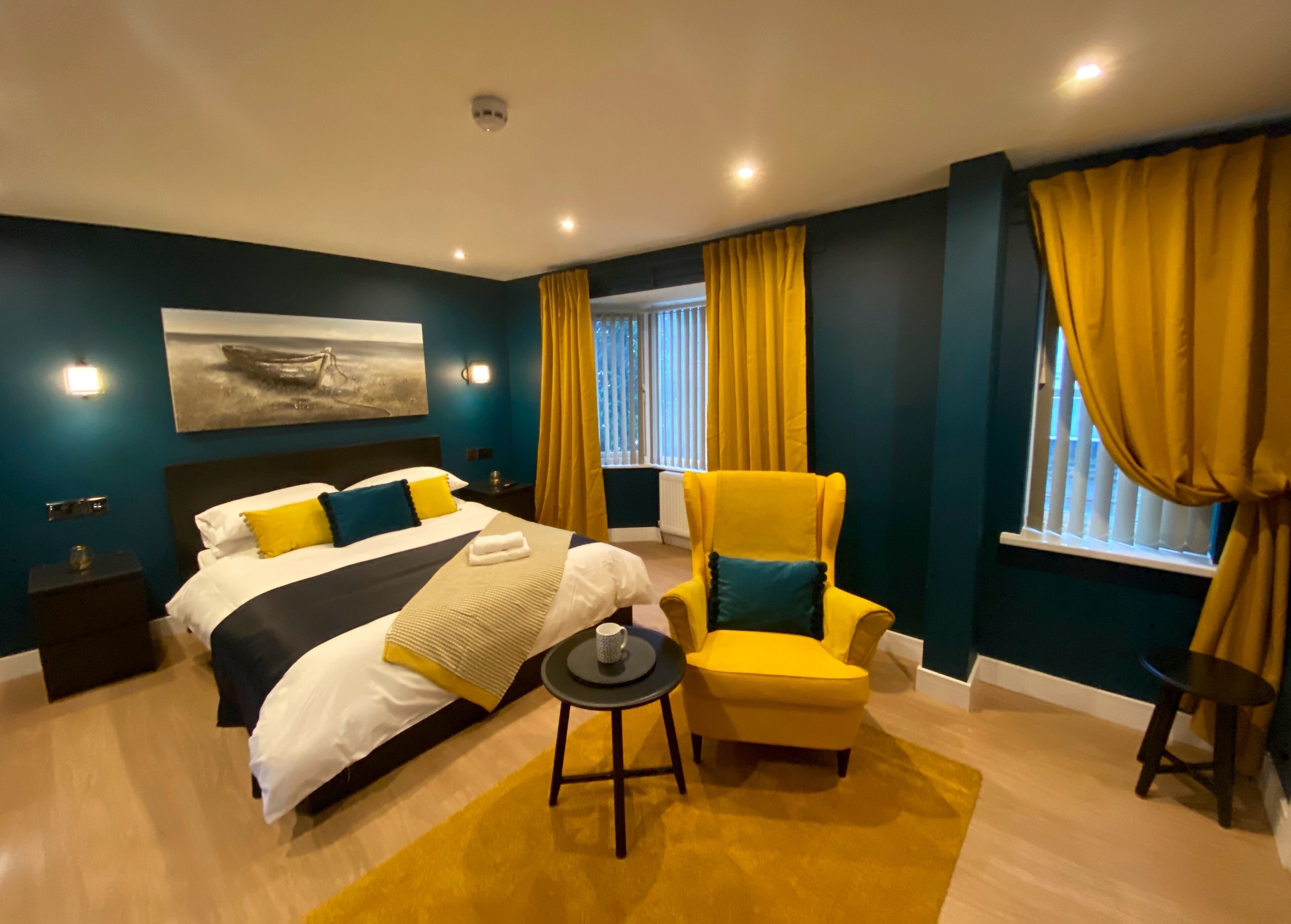 Ein modernes Hotelzimmer mit einem großen Bett, einem gelben Sessel, einem kleinen runden Tisch und einem Bild an der Wand.