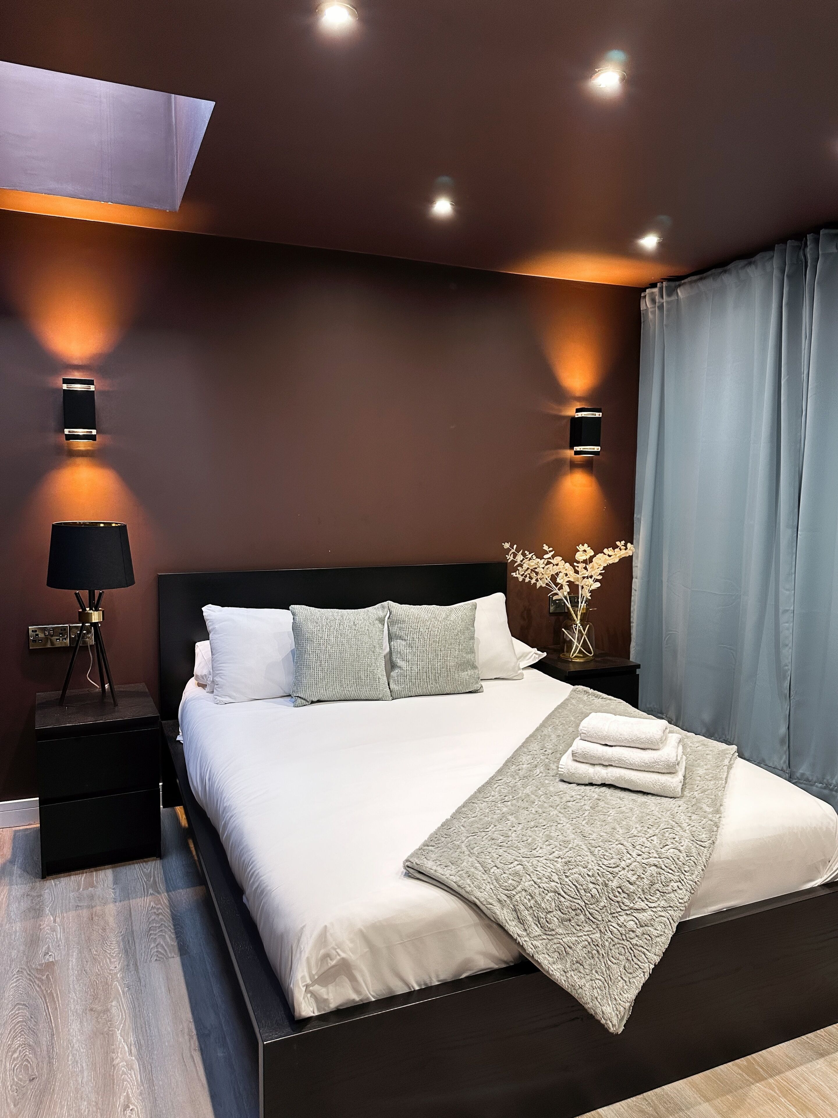 A modern bedroom with a large bed, dark wood headboard, and two bedside tables with lamps.