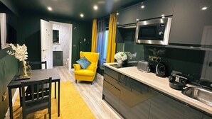 A modern kitchen with a yellow armchair, a dining table, and a microwave. - Sky City Apartments (Coventry)