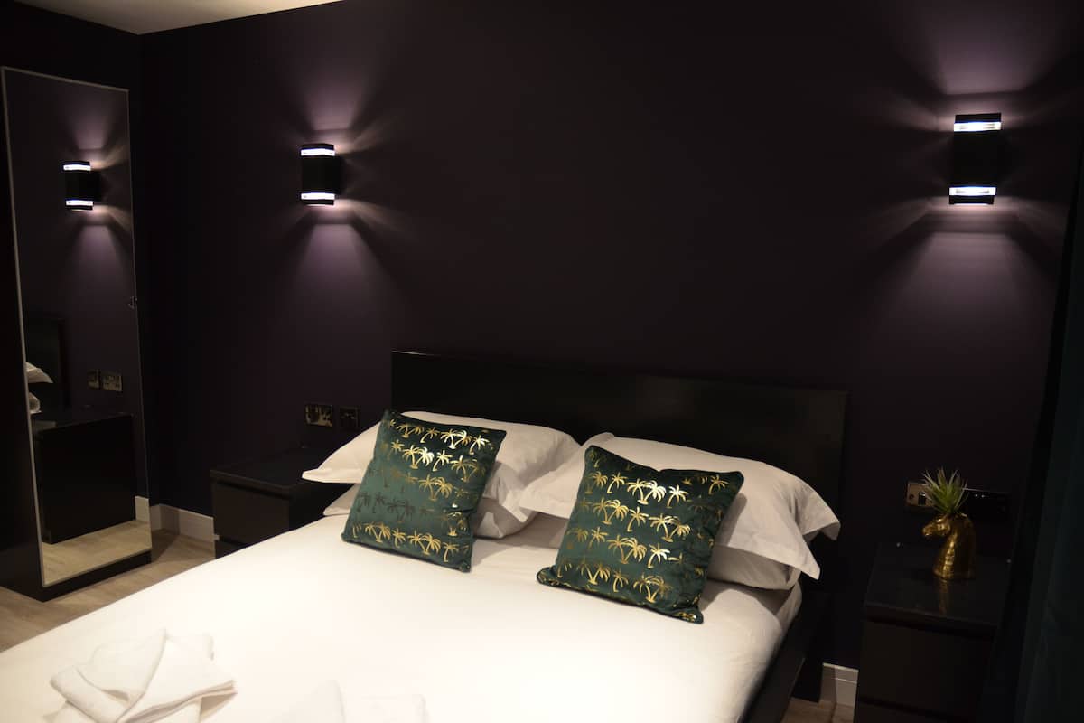 Une chambre d’hôtel moderne avec un grand lit, deux tables de chevet et des lampes fixées au mur.