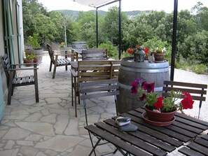 An outdoor patio with wooden benches and tables, surrounded by potted plants and a large barrel. - Le Cadran Solaire (Cabrières)