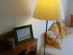 A neatly made bed with floral pillows, a bedside lamp, and a framed picture on a wooden nightstand.