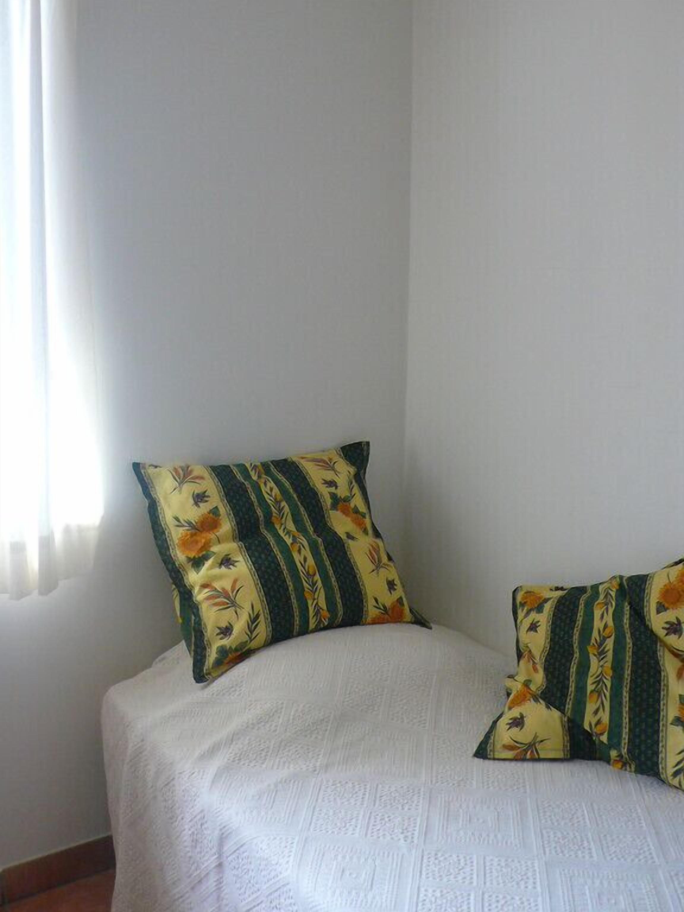 Ein Bett mit weißer, gemusterter Bettdecke und zwei Kissen mit Blumenmuster.