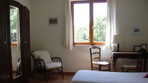Una habitación con una cama, dos sillas, un escritorio, un ventanal con cortinas y una puerta.