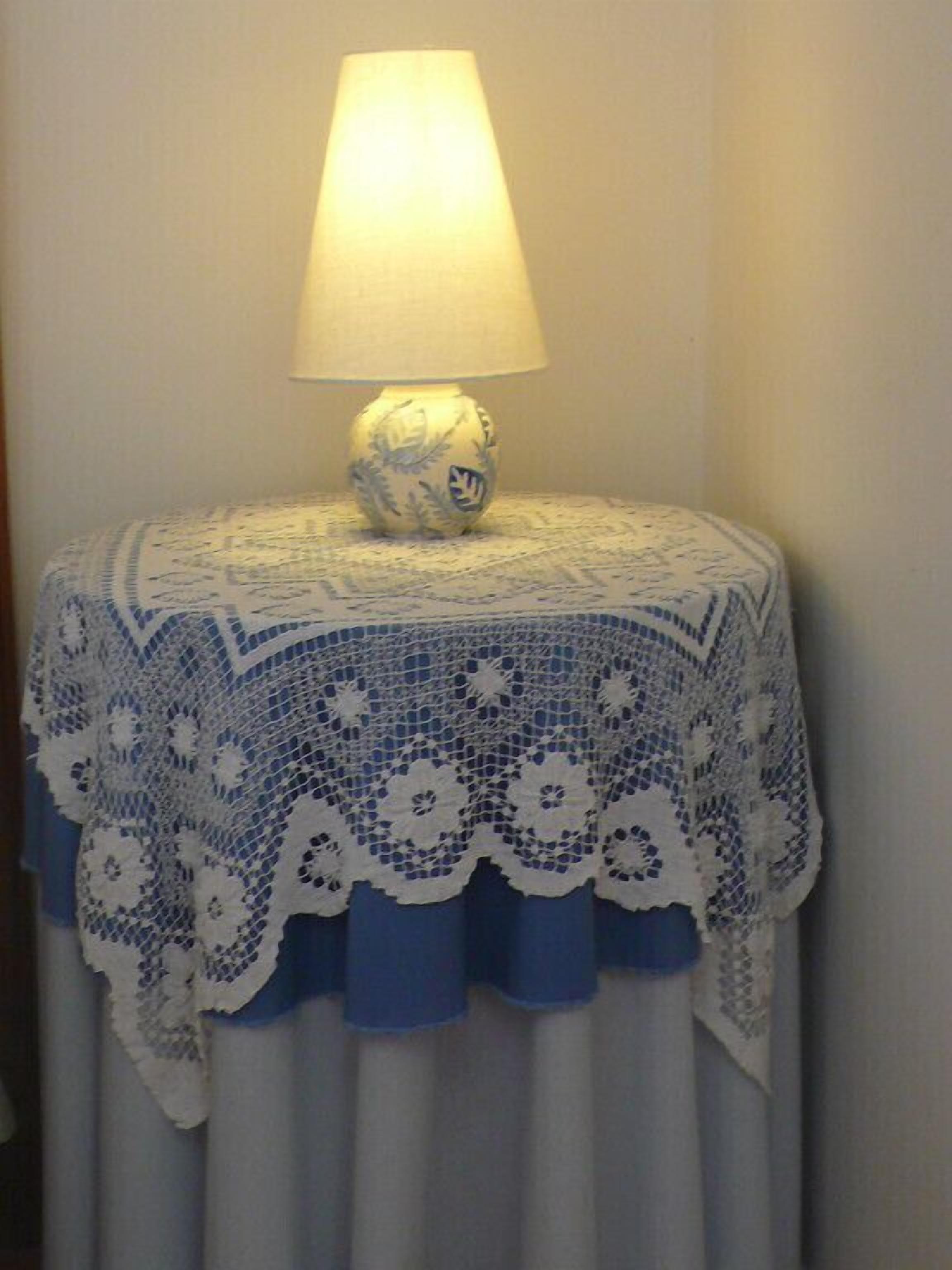 A table with a crocheted tablecloth and a lamp on top.