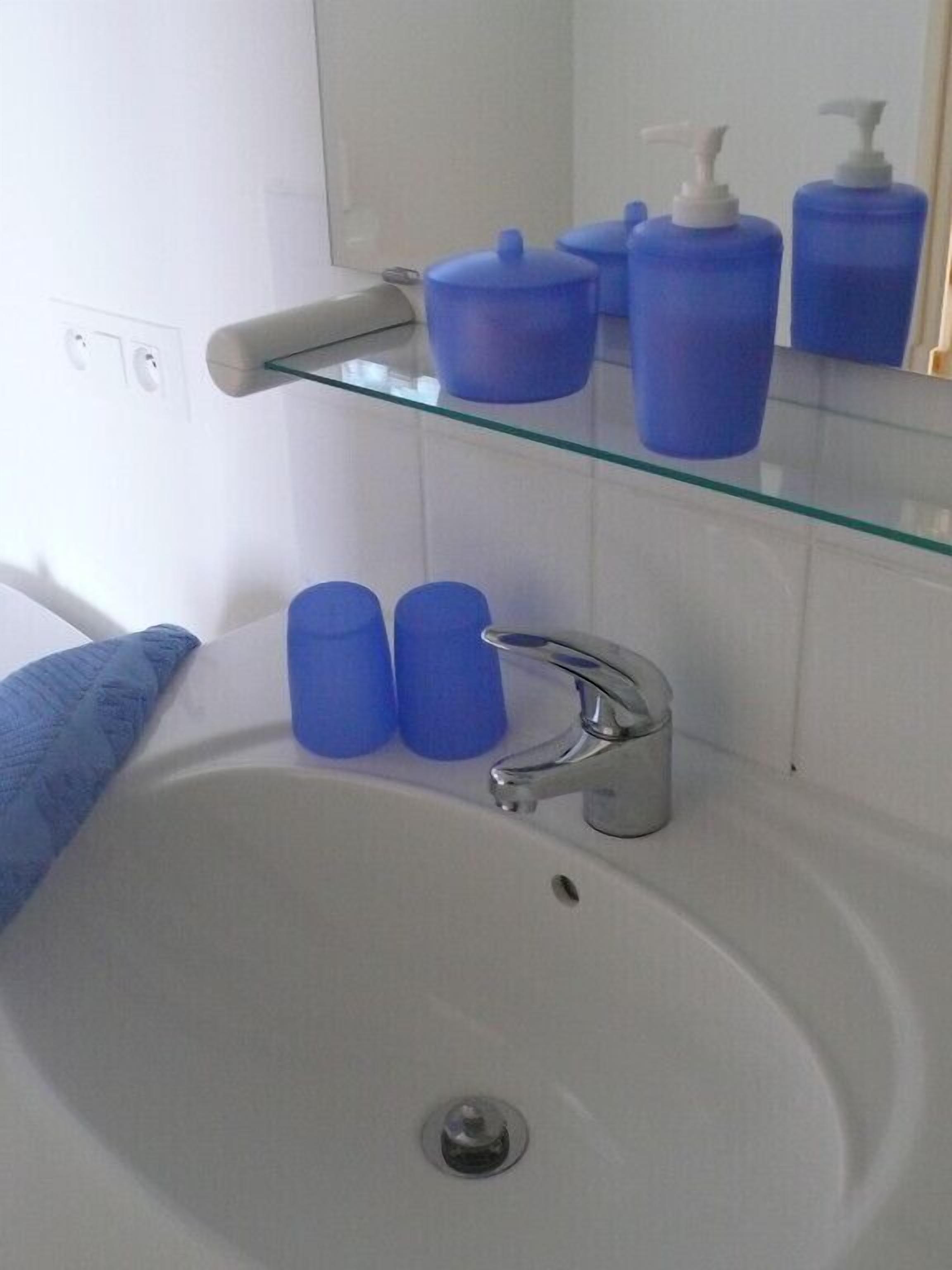 A bathroom with a white sink, a glass shelf holding blue toiletries, and a mirror above the sink.