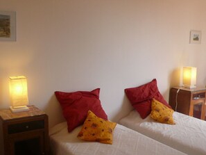A hotel room with two beds, each with a red pillow and a yellow pillow with a pattern. There are bedside lamps on wooden nightstands.