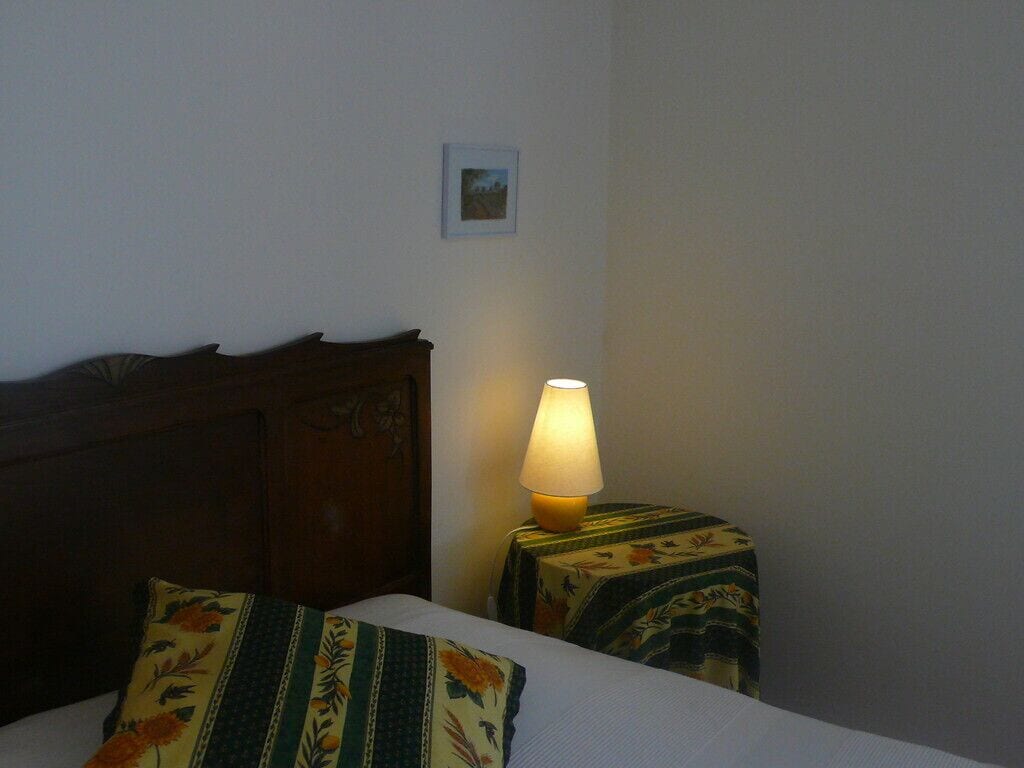 A hotel room with a bed, a nightstand with a lamp, and a small table with a floral tablecloth.