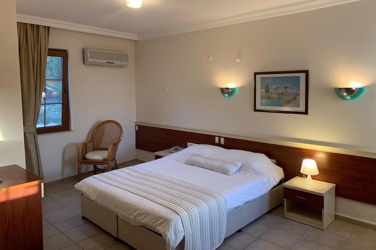 A hotel room with a bed, bedside table, chair, and a painting on the wall.