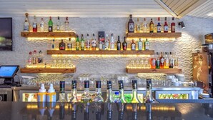 Baaritiskialue, jossa on useita hyllyjä täynnä alkoholijuomapulloja ja laseja, kassakone ja tietokonenäyttö.