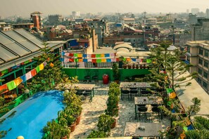 A rooftop terrace with multiple tables and chairs, surrounded by potted plants and colorful flags. - Nepal Ayurveda Home (Kathmandu)