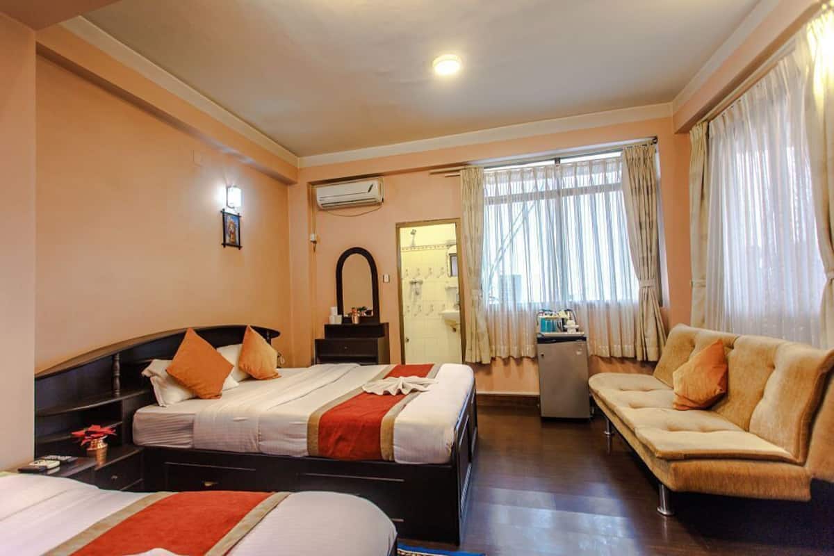 A hotel room with two beds, a sofa, a desk, and a bathroom visible through a door.