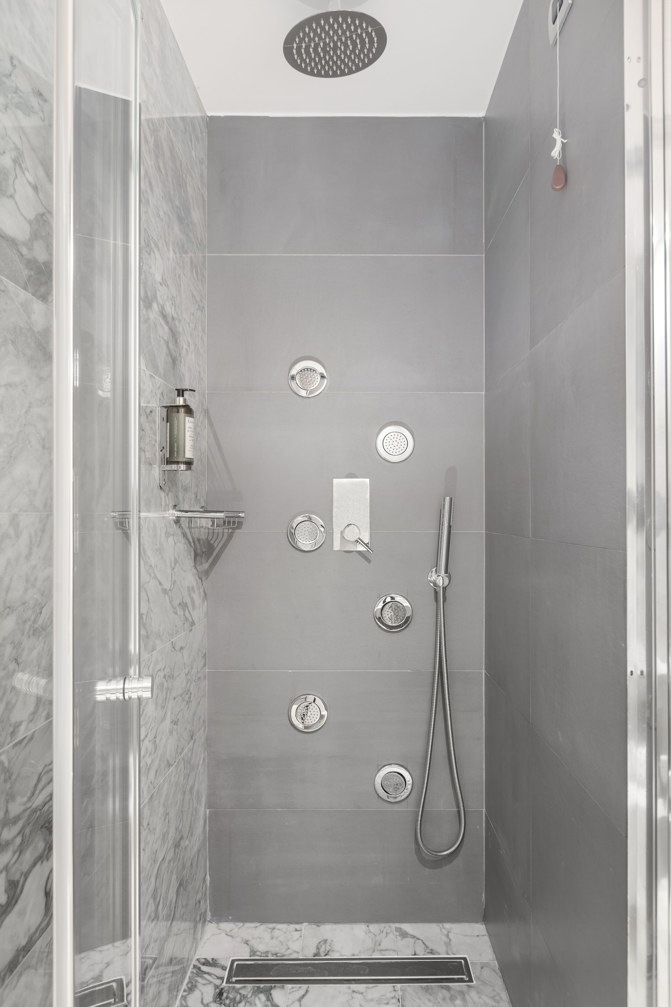 Une douche moderne dotée d’une paroi en verre, d’un pommeau de douche à main et d’un robinet mural.