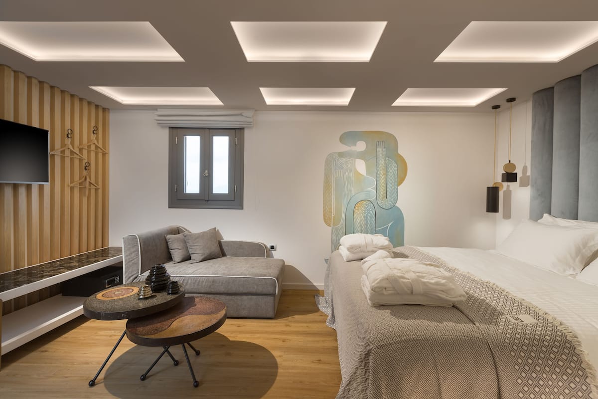 Un dormitorio moderno con cama, sofá, una mesita y televisor montado en la pared.