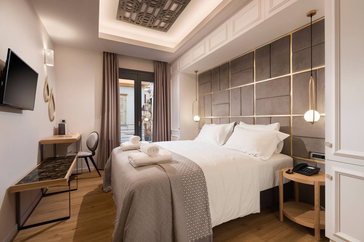 Una habitación de hotel moderna con una cama grande, un escritorio, una silla, un televisor y un teléfono sobre una mesita de noche.