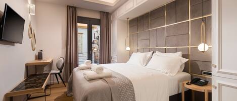A modern hotel room with a large bed, a desk, a chair, a TV, and a phone on a side table.