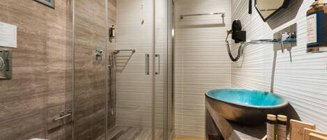A modern bathroom with a glass-enclosed shower, a large blue sink, and a wooden vanity.