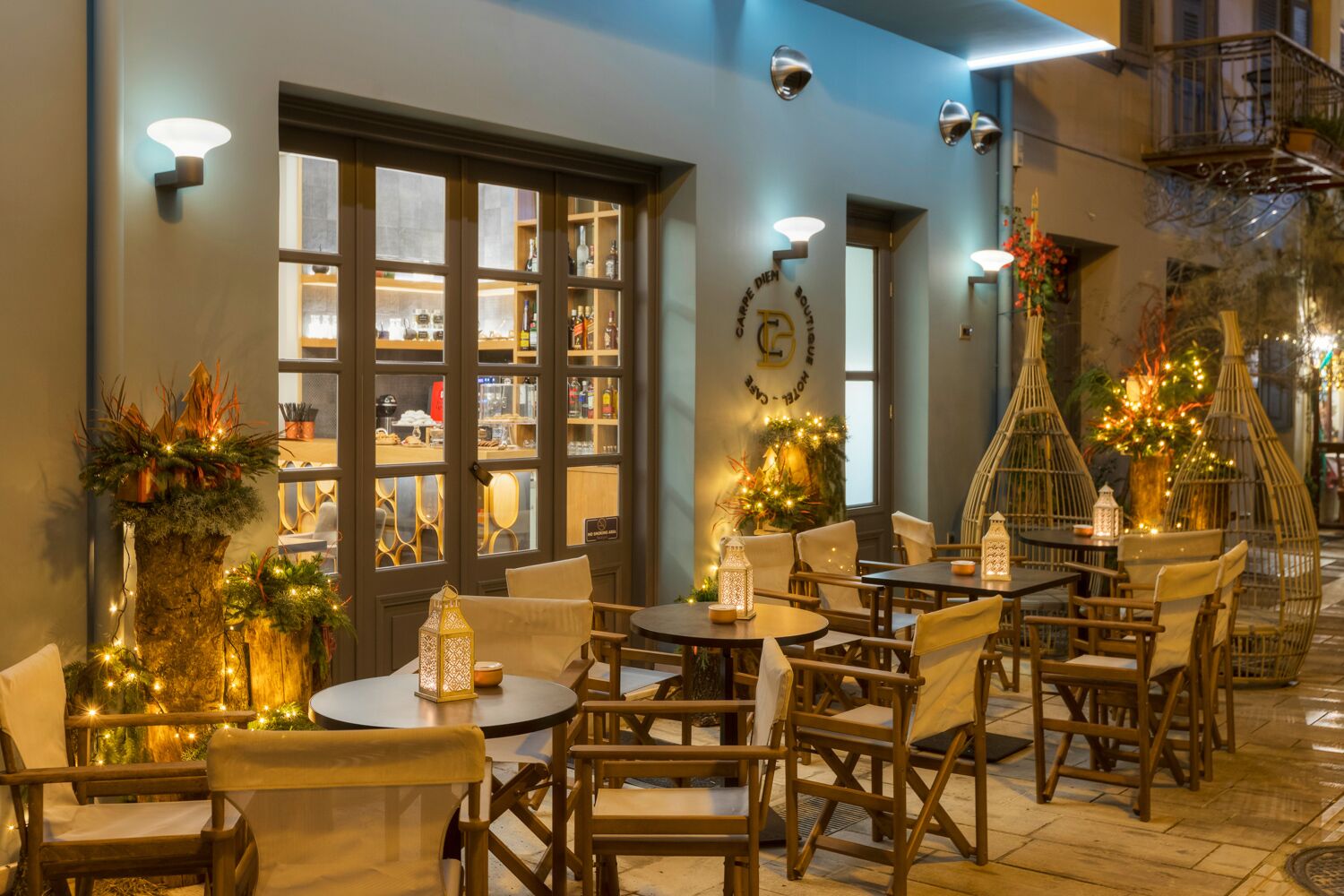 An outdoor seating area with tables and chairs, a bar visible through a glass door, and decorative lights.